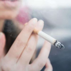 A close up of a cigarette held by a woman. Her face is in a blurred background