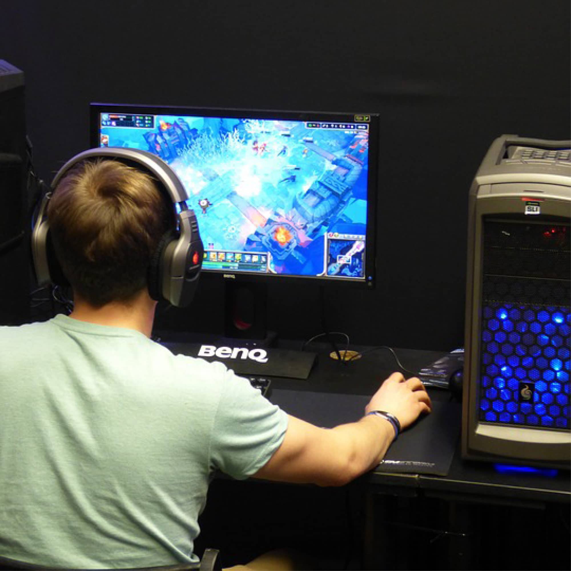 A person sitting at a computer with their back to the camera. They are wearing headphones and their right hand is resting on a mouse