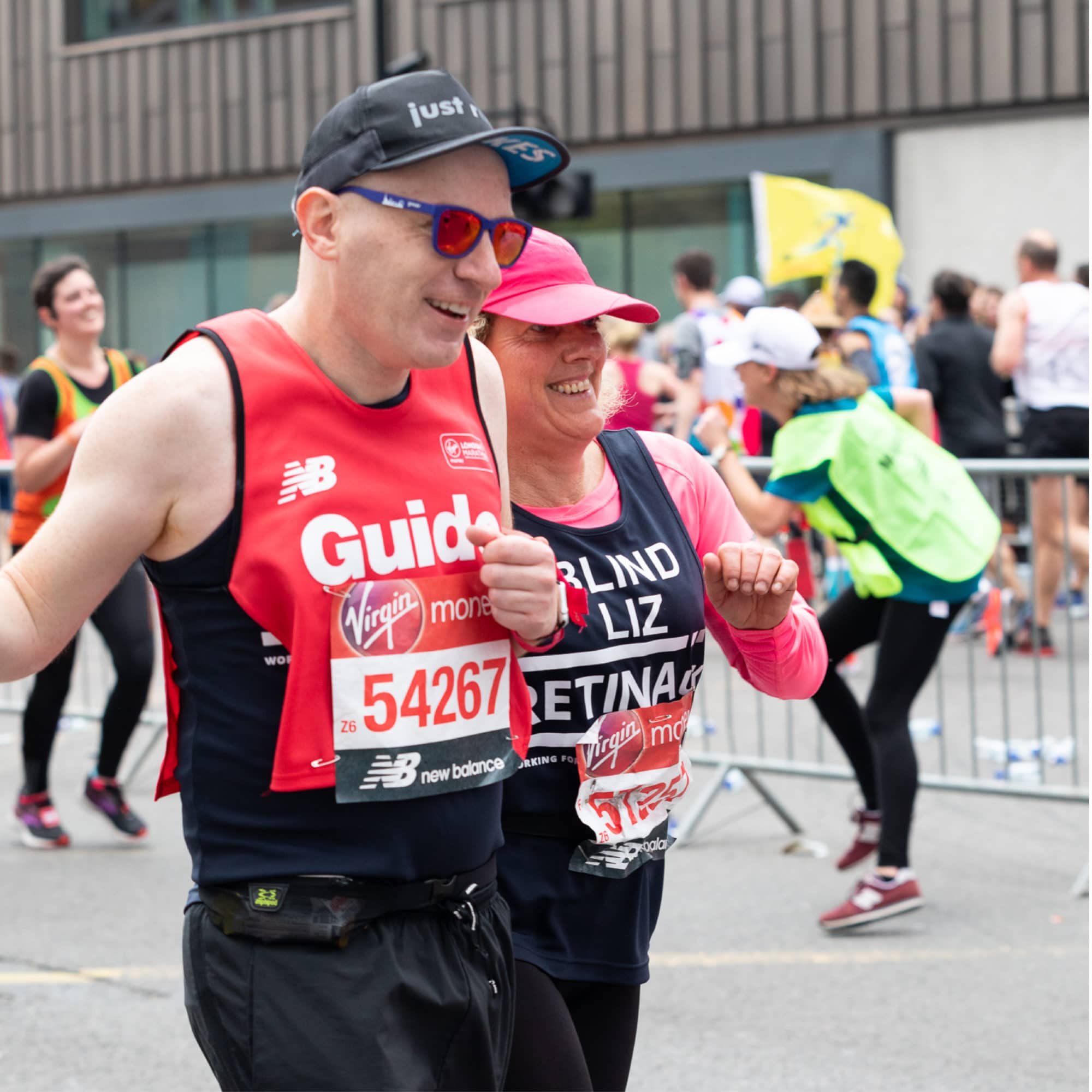 Image shows a runner in a red vest with 'guide' written on the front running alongside a Retina UK runner in a blue charity running vest.