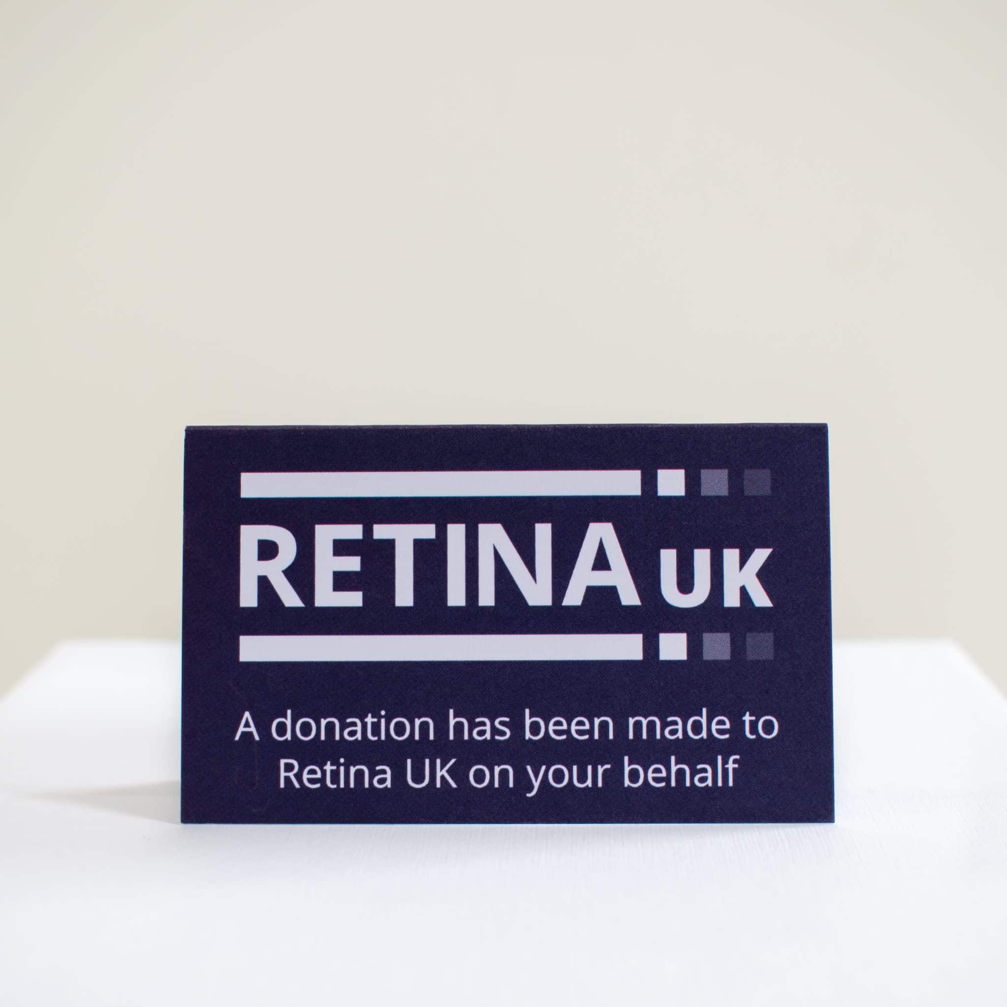A tented card viewed straight on with the Retina UK logo and the words "A donation has been made to Retina UK on your behalf" in white on a blue background.