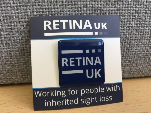 The Retina UK Pin badge mounted on a card with the words 'Working for people with inherited sight loss' printed on the card below the badge