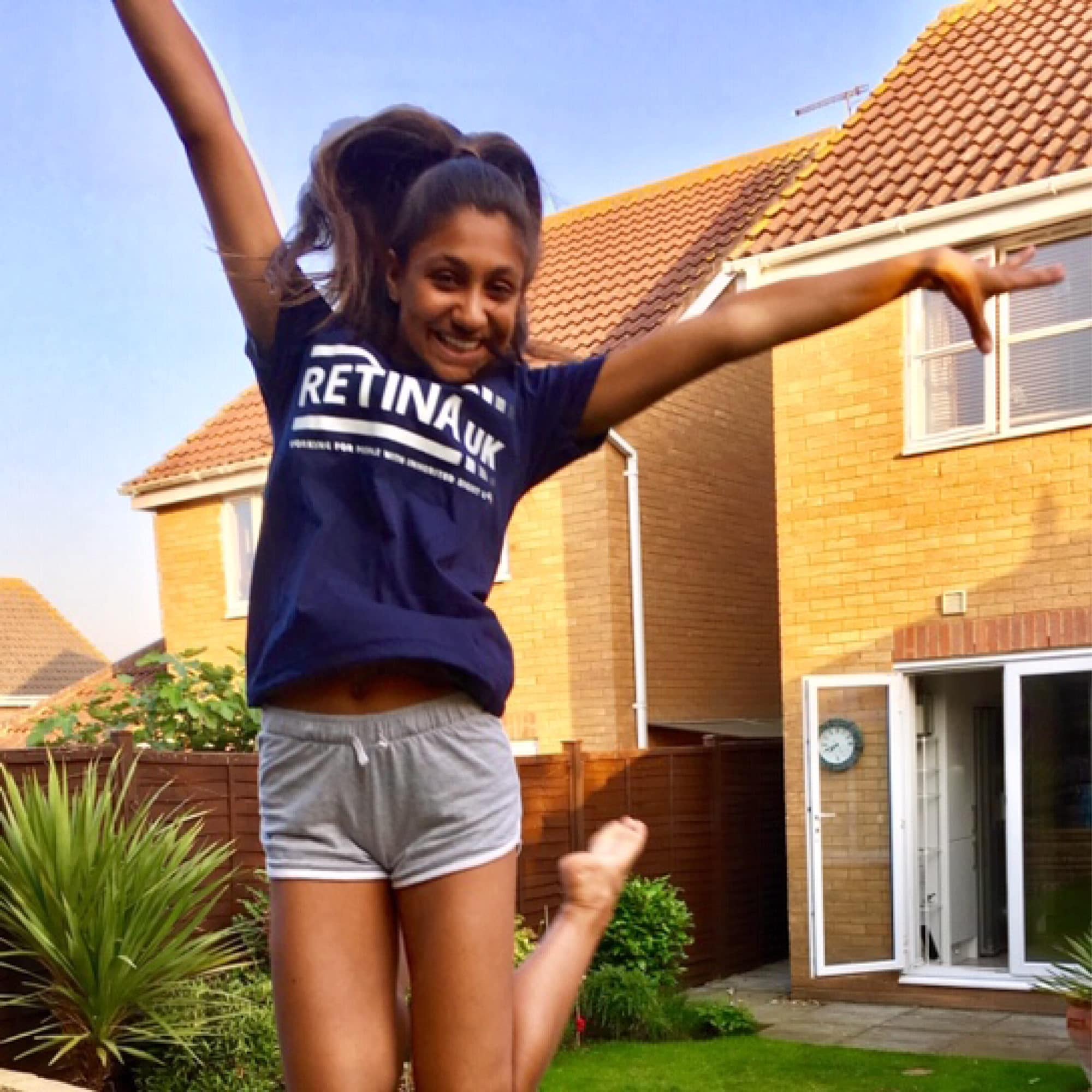 Image shows a young girl in a blue Retina UK t-shirt jumping into the air and smiling