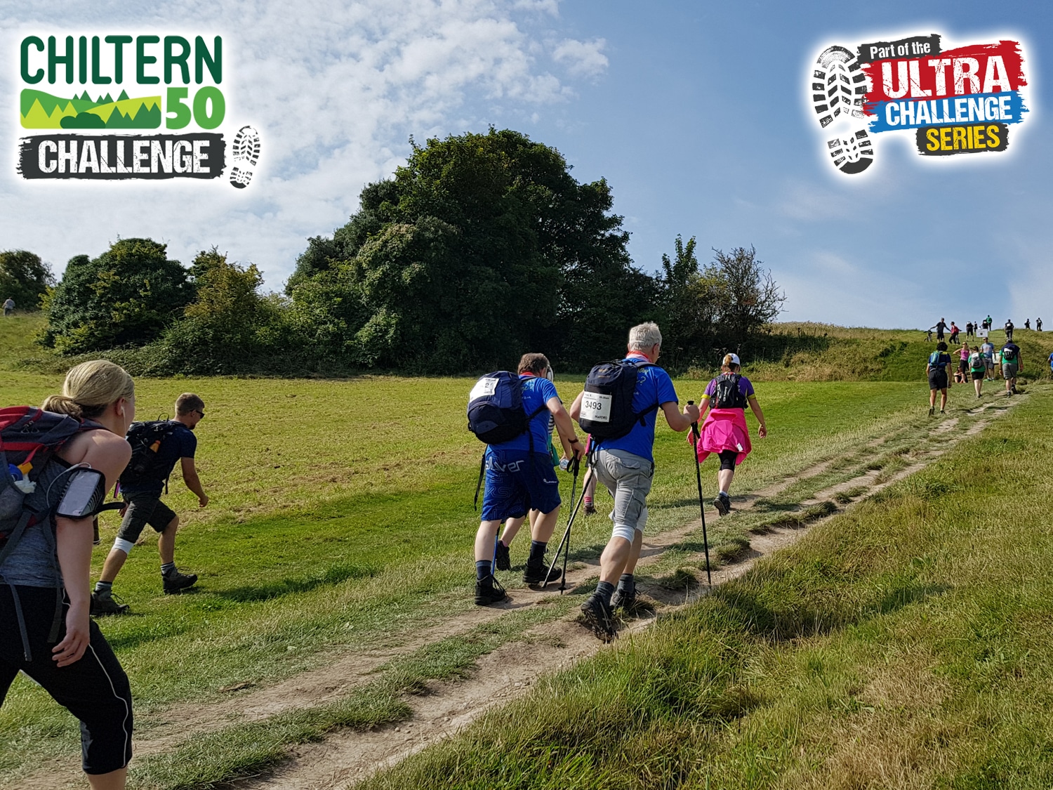 Image shows a group of walkers following a trail to the top of a hill. Trees and green fields line the trail.