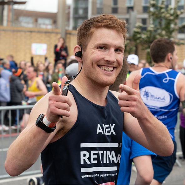 A runner is shown in a Retina UK runnning vest posing with a thumbs up