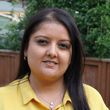 An Asian woman looking at the camera. She is wearing a yellow shirt and her hair is falling over her left shoulder