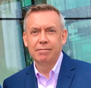 Martin Kirkup - a man with greyind hair to his tempes. He is wearing a navy suit jacket and a light lavender coloured shirt with an open collar