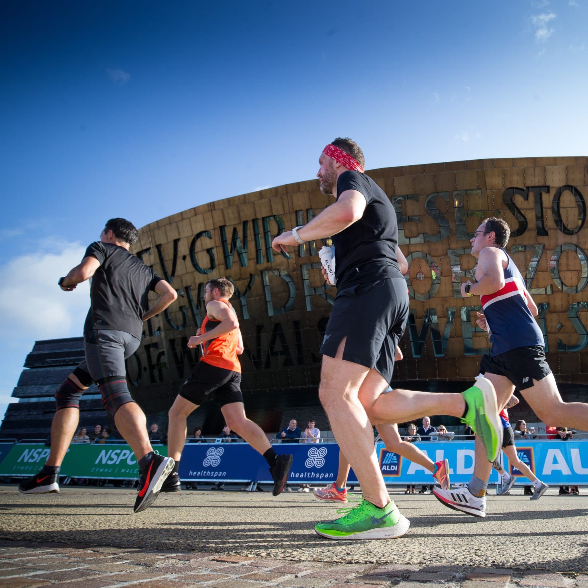 Image shows a group of runners running in front of the Wales Millennium Centre