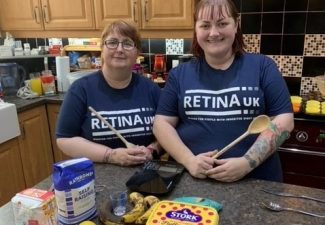 image shows two supporters stood next to each other in a kitchen smiling. Both are wearing blue Retina UK t-shirts and are holding wooden mixing spoons