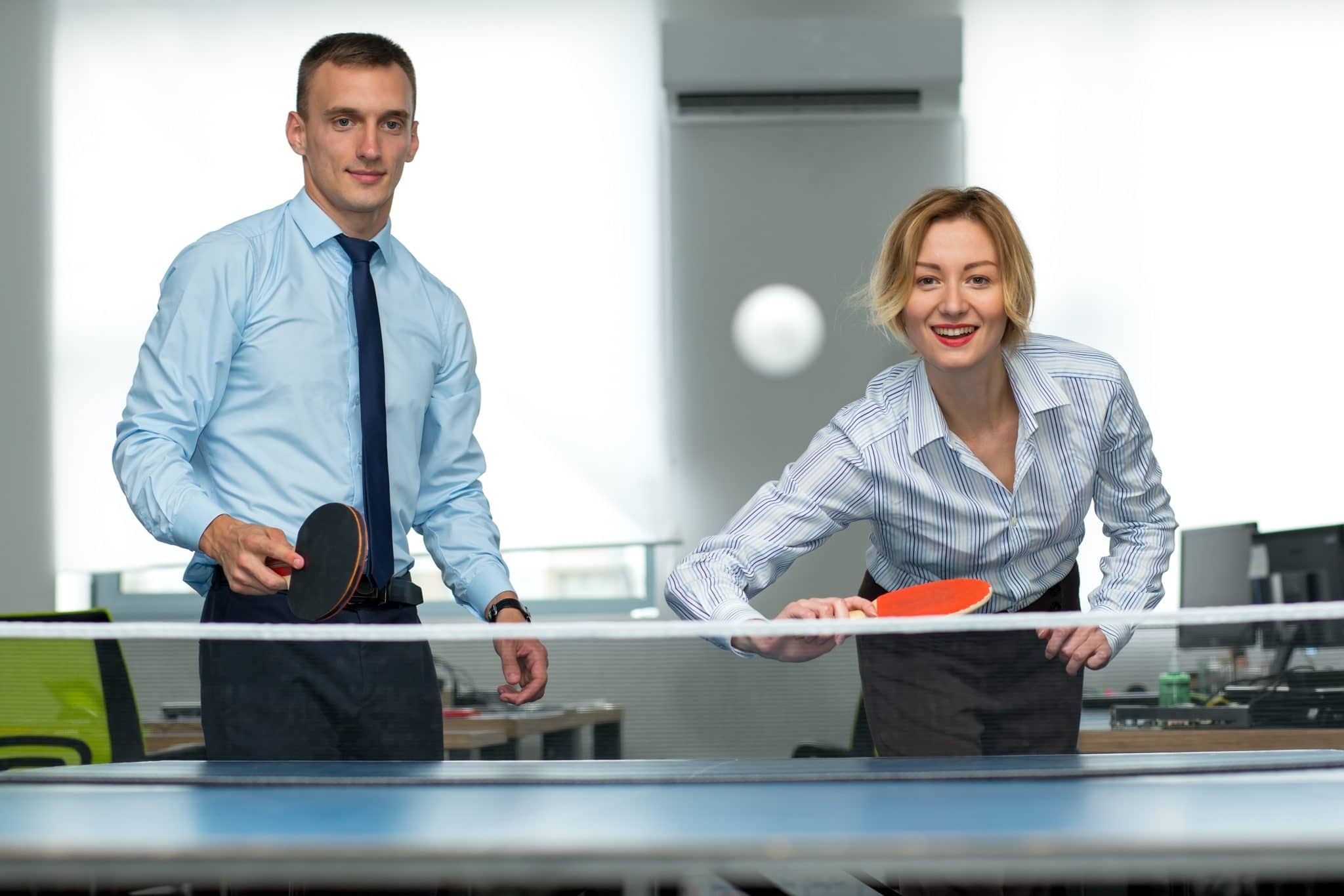 A man and a woman wearing smart clothes playing table tennis