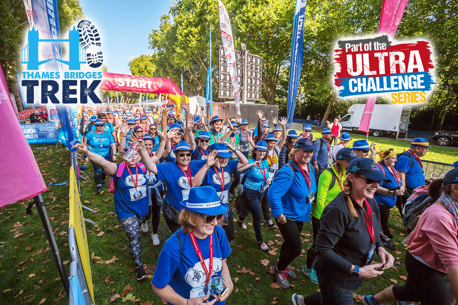 Image shows a crowd of walkers in blue t-shirts walking across the start line. Trees line the route. The 'Thames Bridges Trek' logo is in blue a the top left. The top right reads 'part of the Ultra Challenge Series'