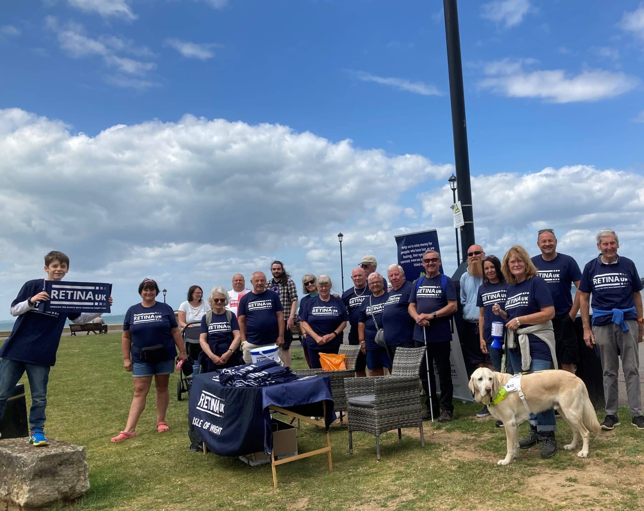 Image shows a large group of people stood on a grassed area. Most are wearing blue Retina UK t-shirts. Blue sky is visible behind them.