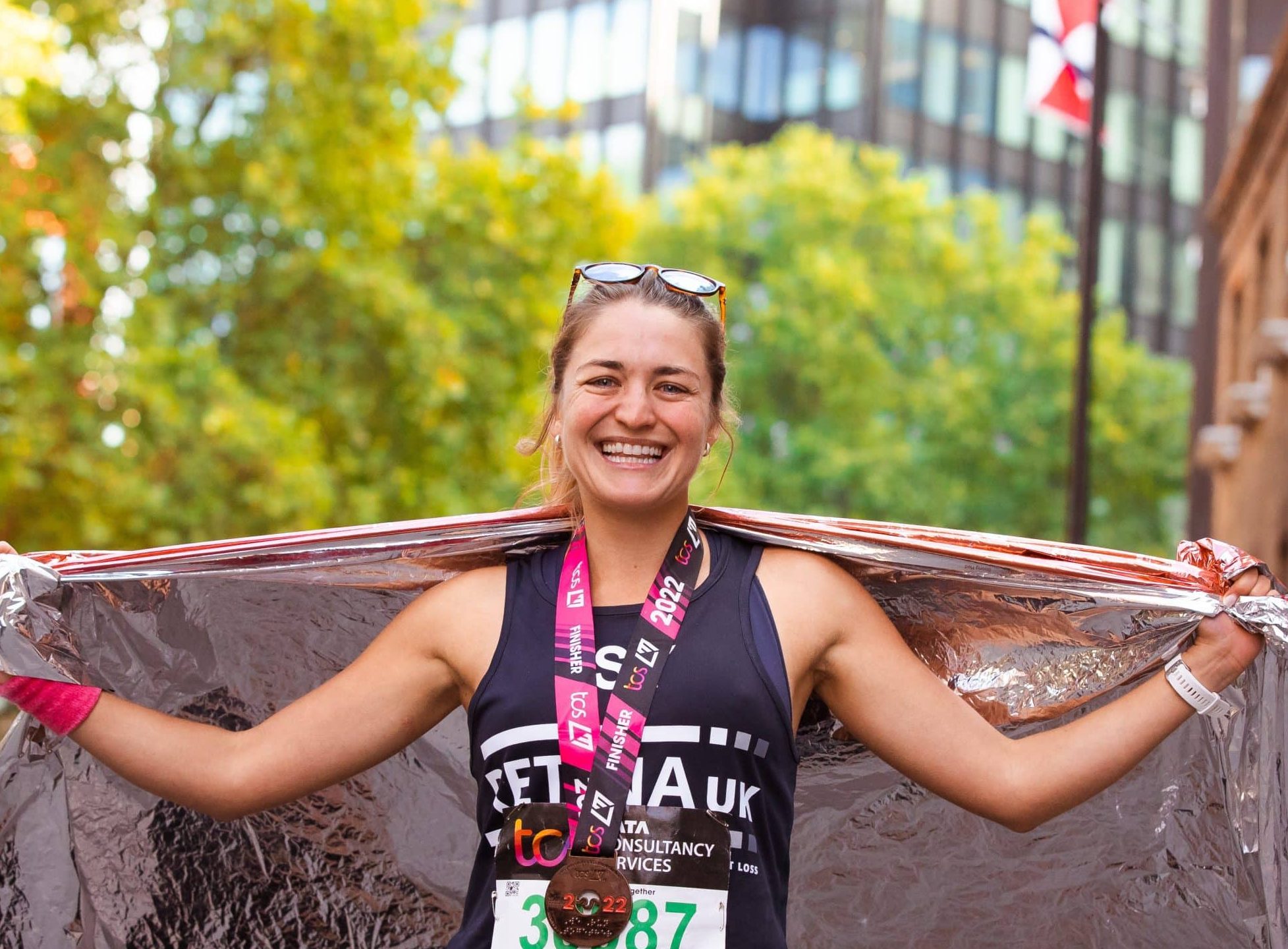 Image shows a runner stood smiling with her arms outstretched . She is wearing a blue Retina UK running vest and a London Marathon medal around her neck.