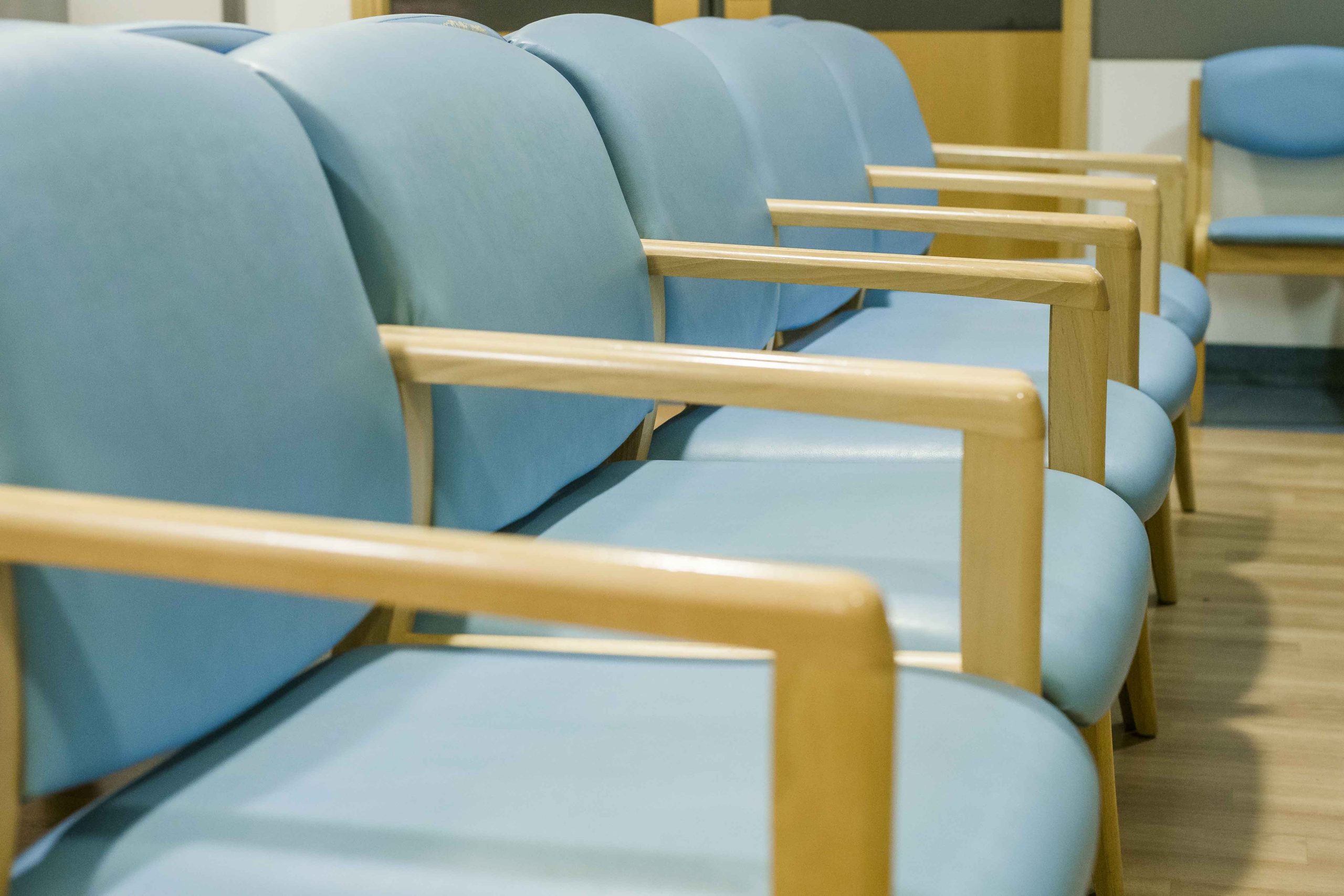 A row of chairs with wipeable blue green covers set in an eye clinic waiting room