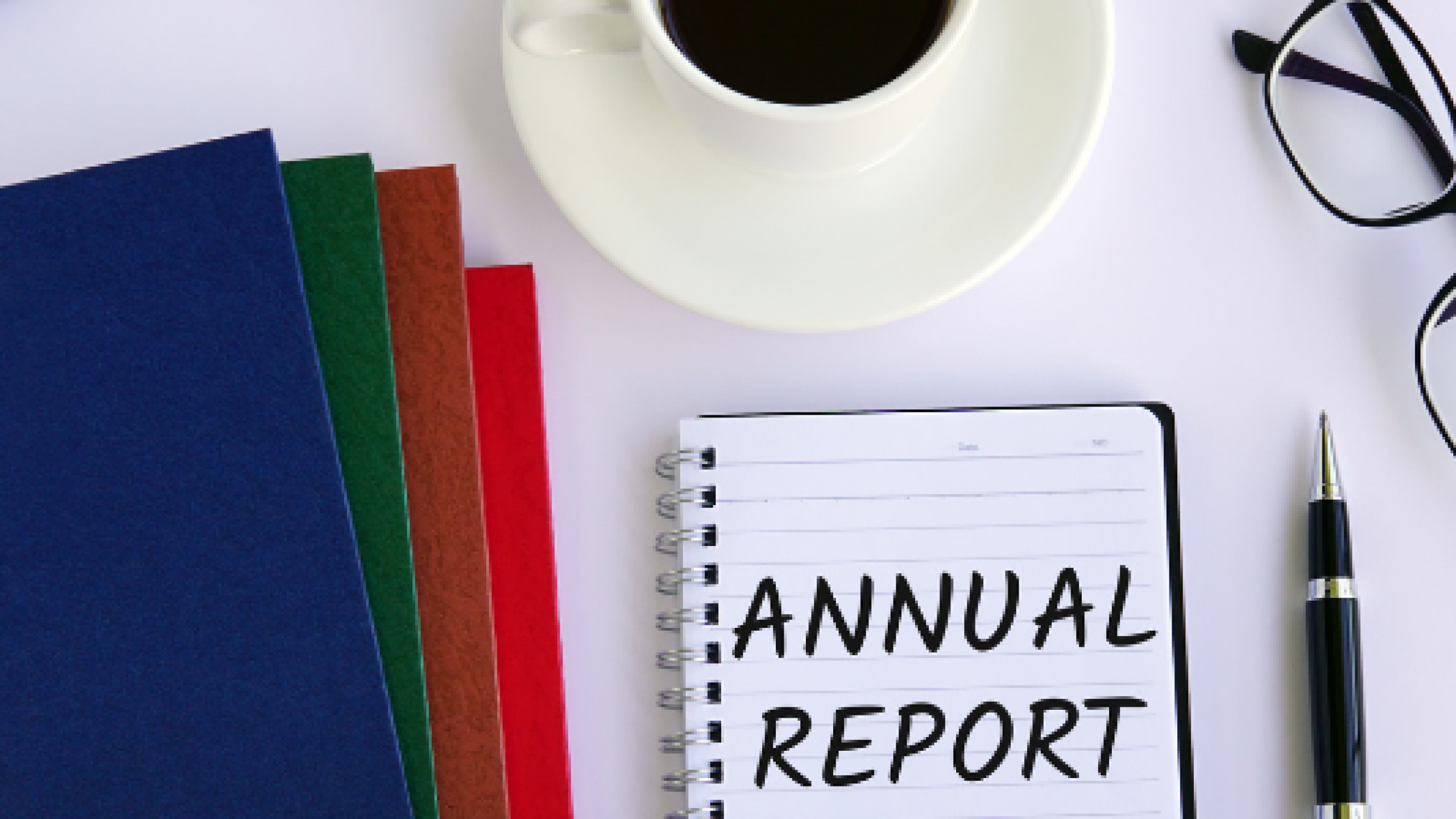 Annual Report with a cup of black coffee and four folders on a desk