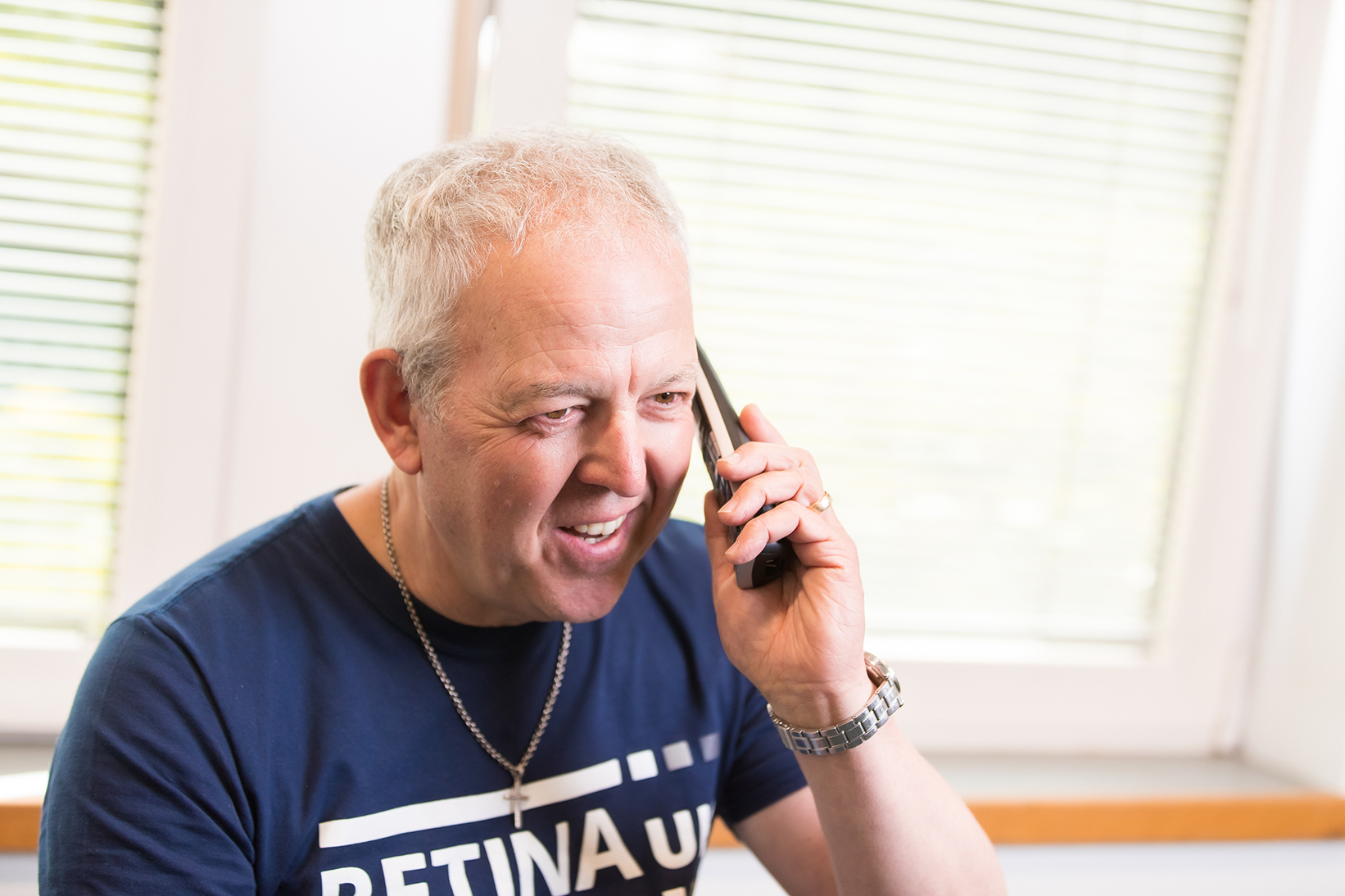 A man wearing a Retina UK tshirt holding a phone handset to his left ear