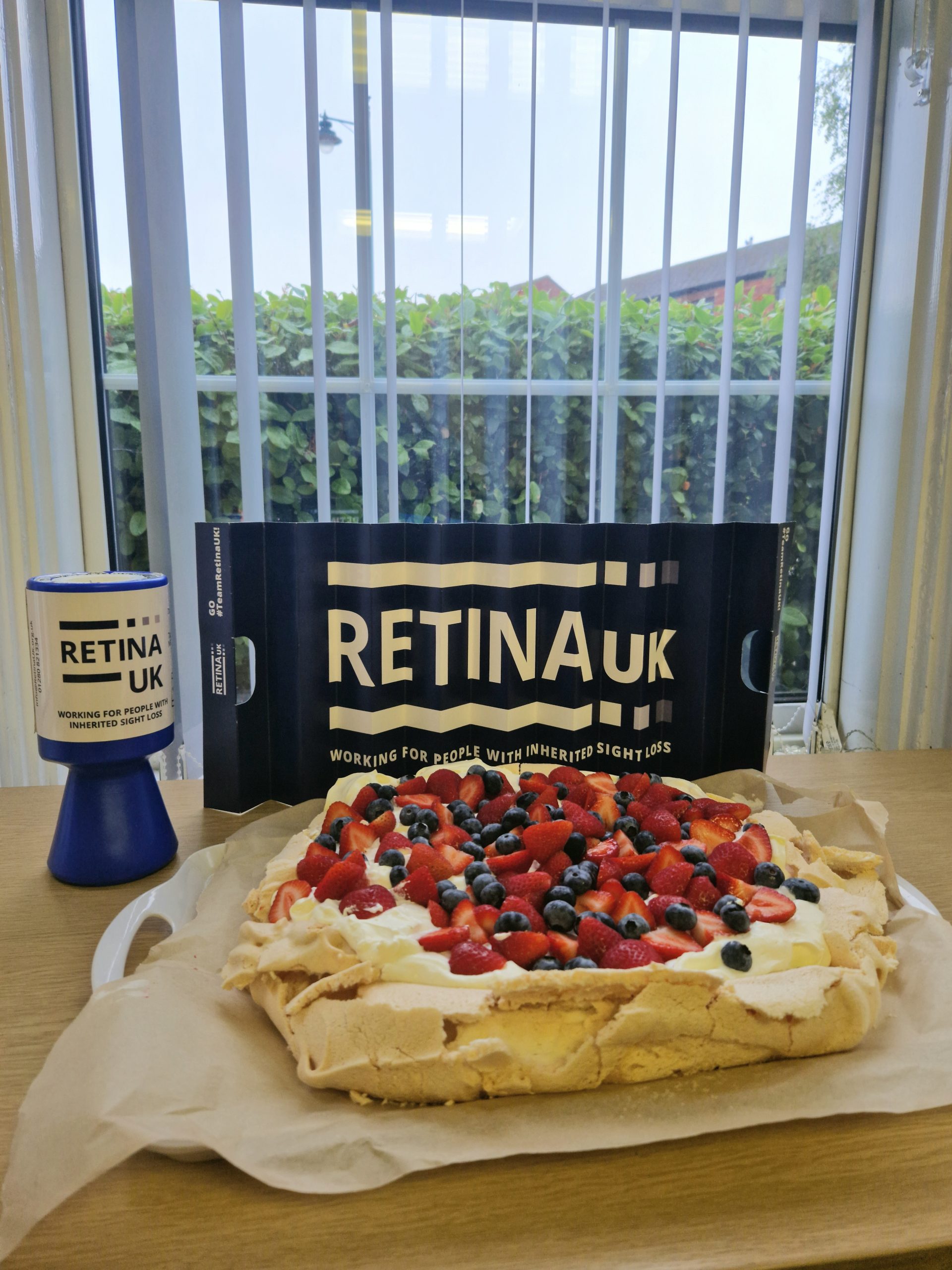 A fruit pavlova with a Retina UK collecting tin at the rear of the picture