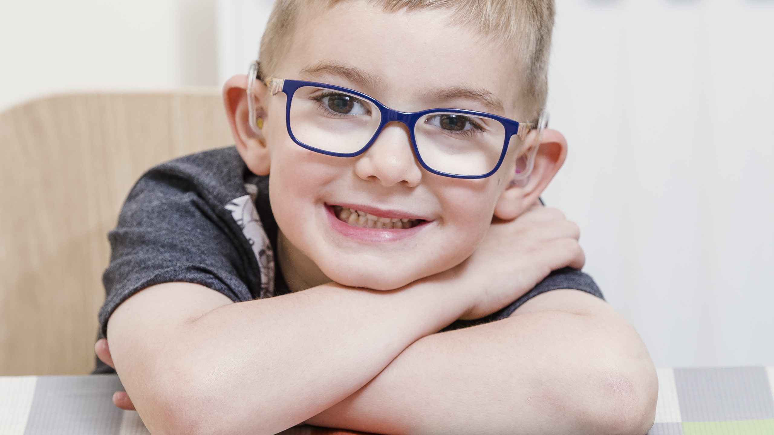 A young boy wearing glasses with his arms folded on a table