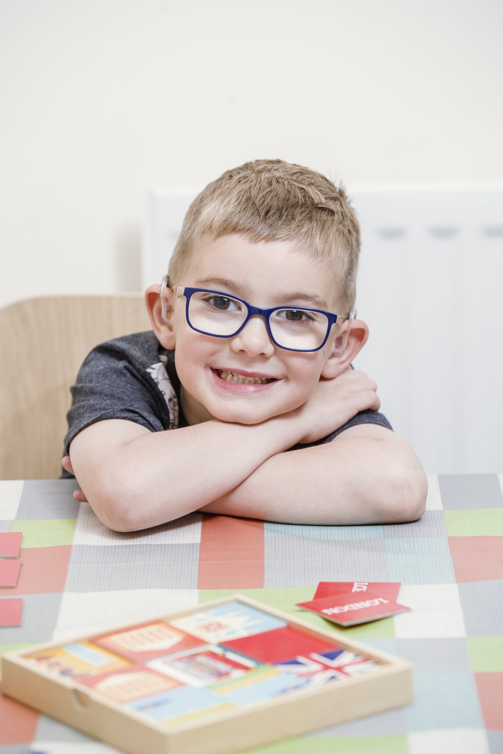 A young boy wearing glasses with his arms folded on a table