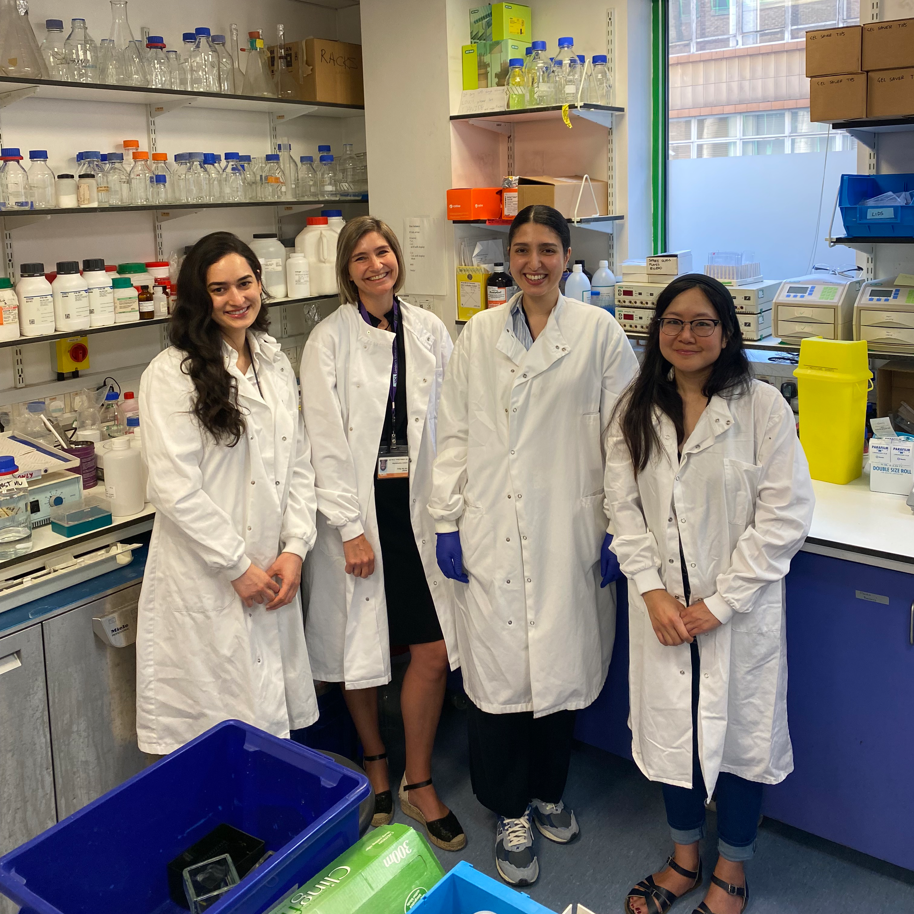 Four women in a research lab. They are all wearing white lab coats