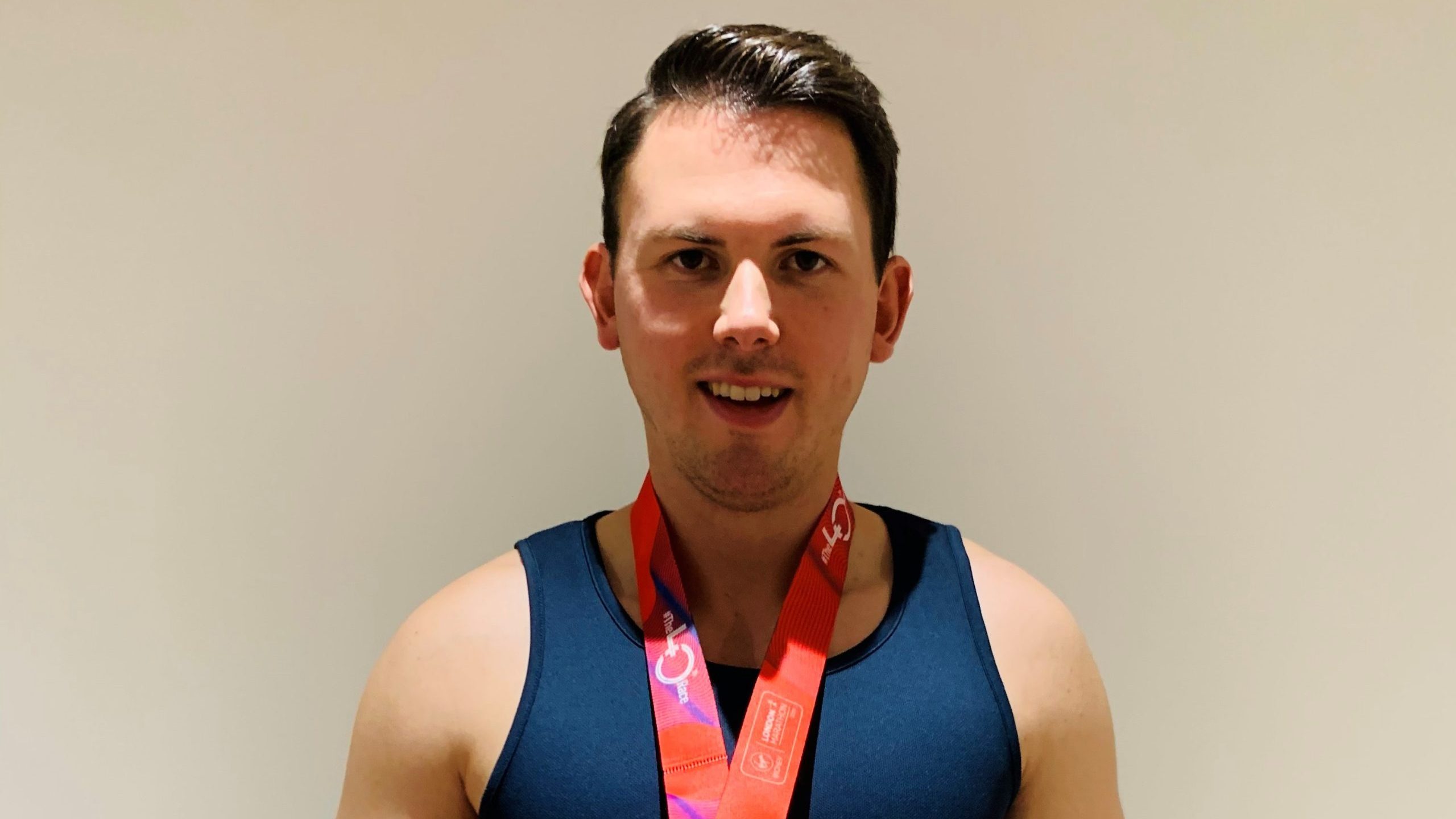 James standing facing the camera. He is wearing a Retina UK running vest and has a medal around his neck.