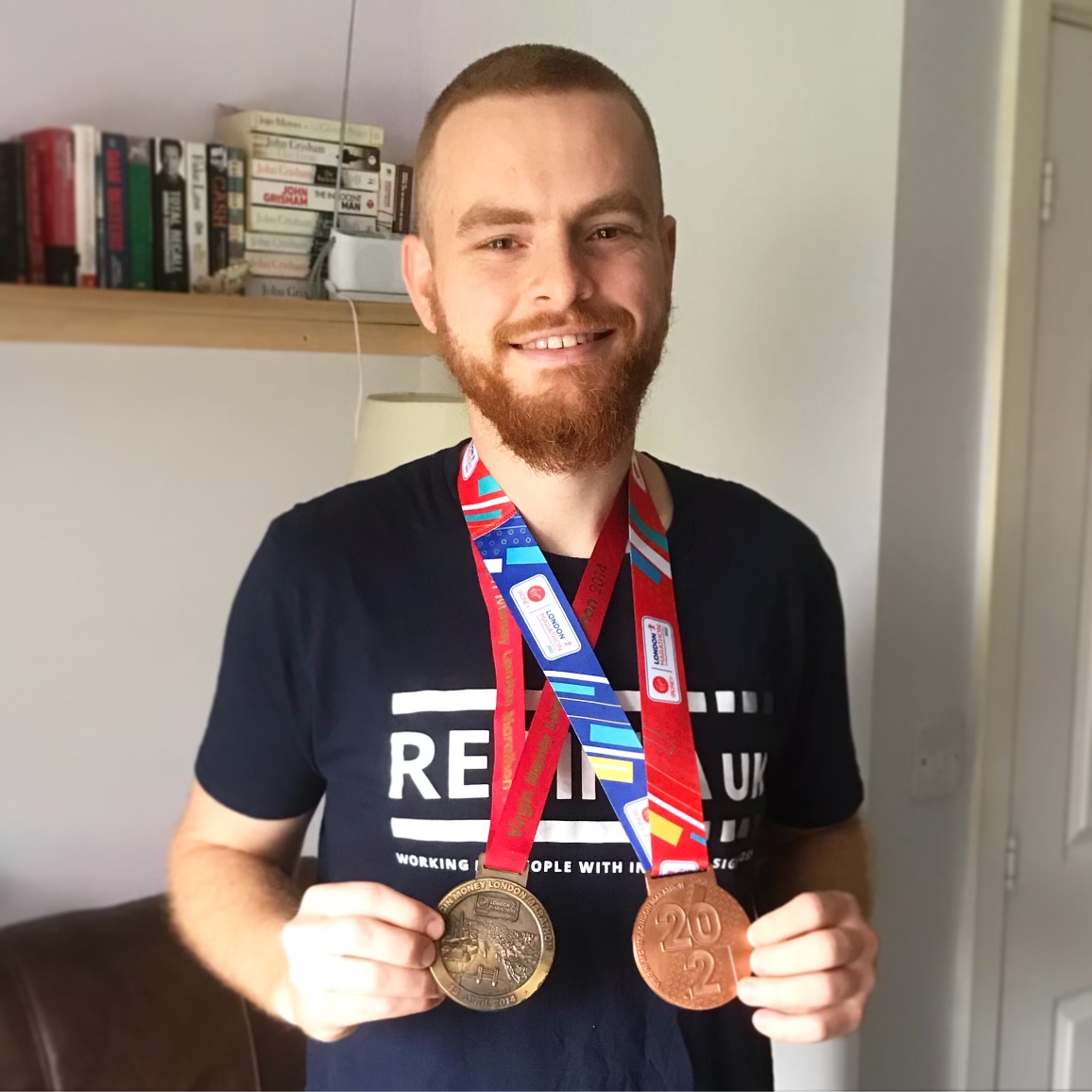 William, smiling directly at the camera. He is wearing a Retina UK tshirt and has two medals hanging around his neck