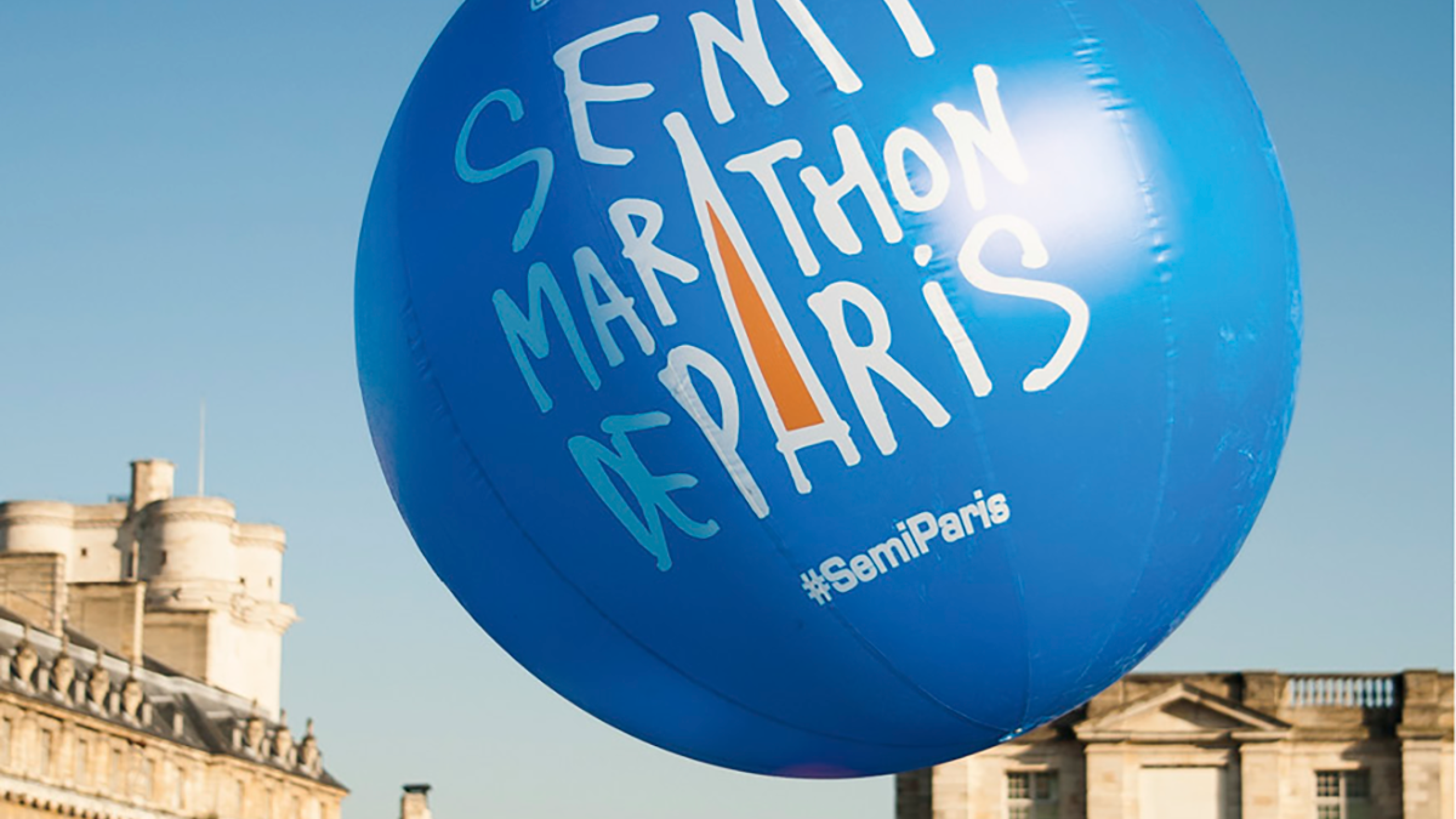 A view of runners assembling in a square with a big blue balloon which says 'Semi Marathon De Paris'