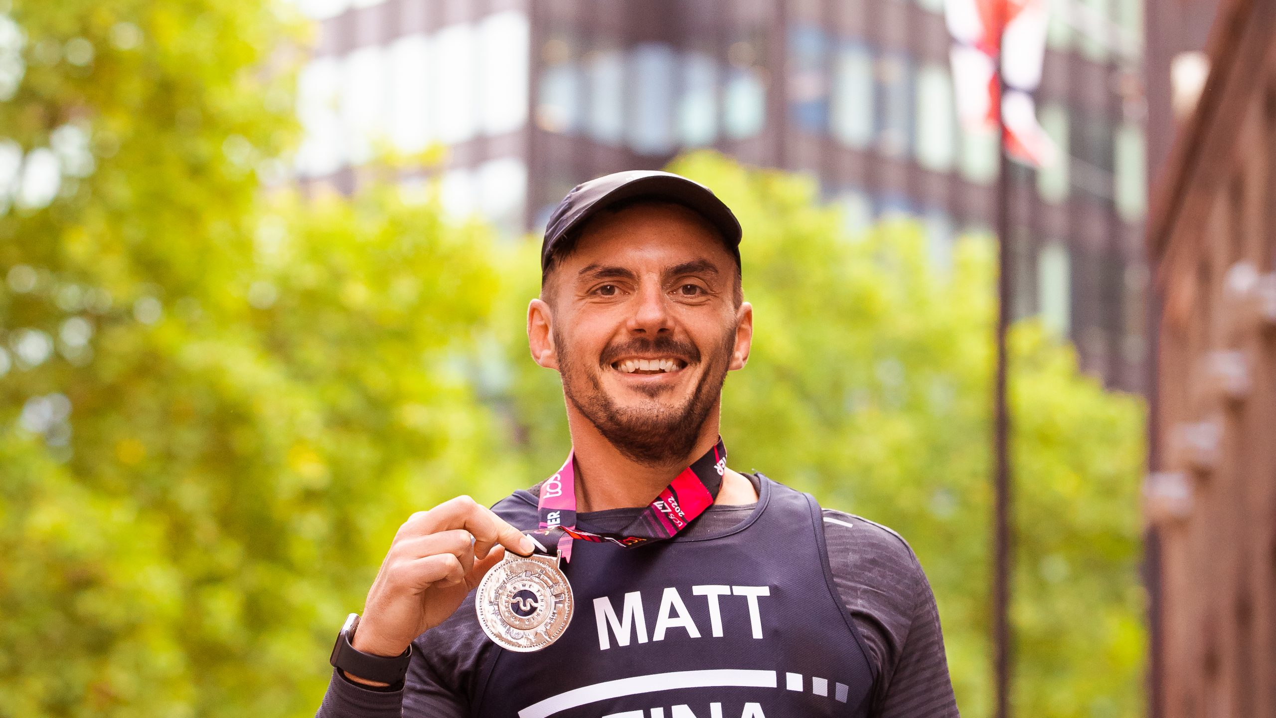 A male runner smiles as he holds his London Marathon medal.
