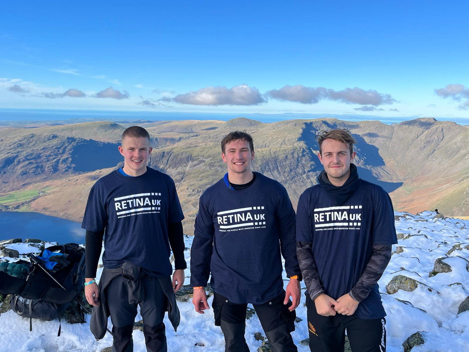 Three men wearing Retina UK t-shirts, standing on top of a mountain