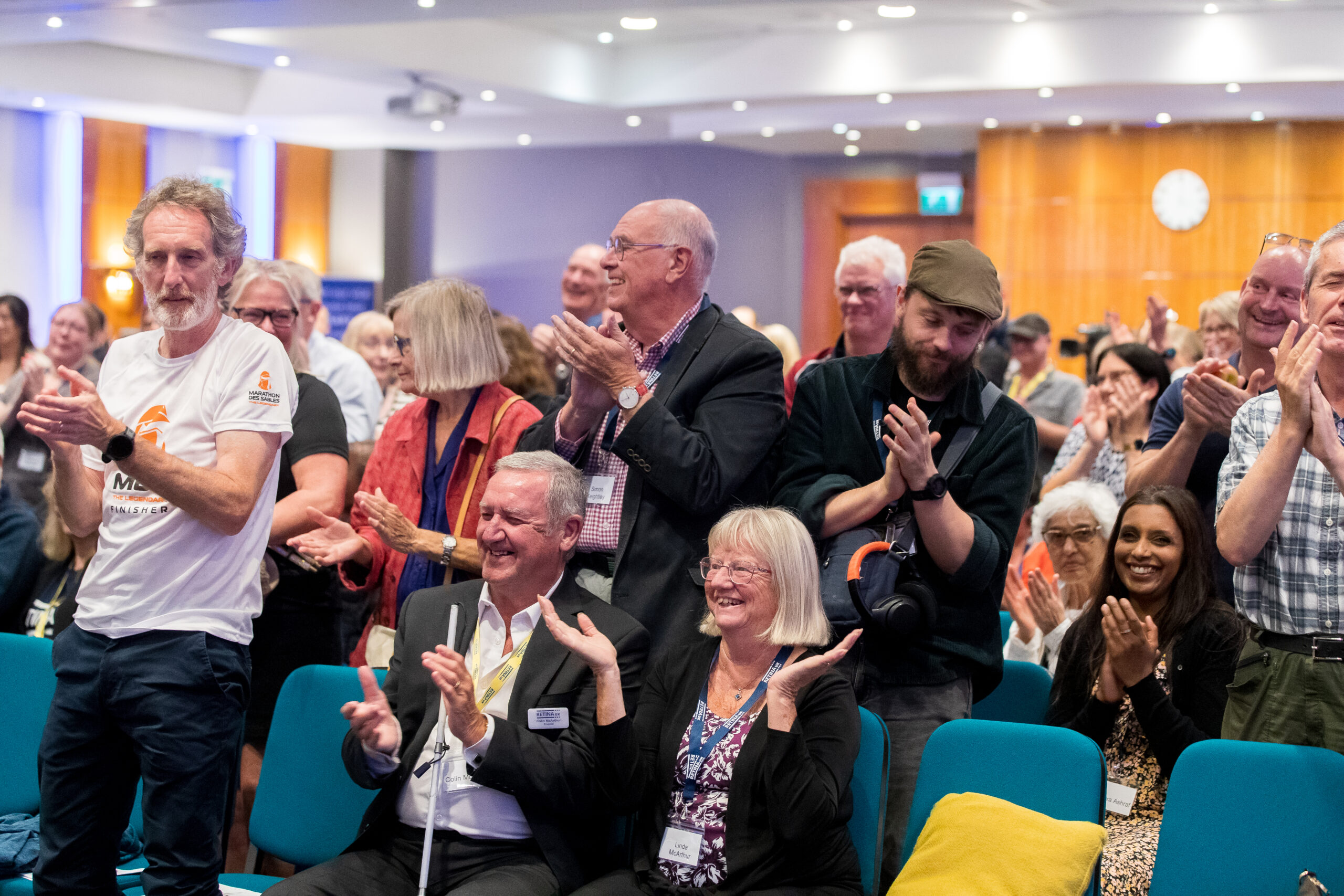 Image shows audience members from 2025 annual conference. Audience are sat and stood applauding and smiling at the stage.