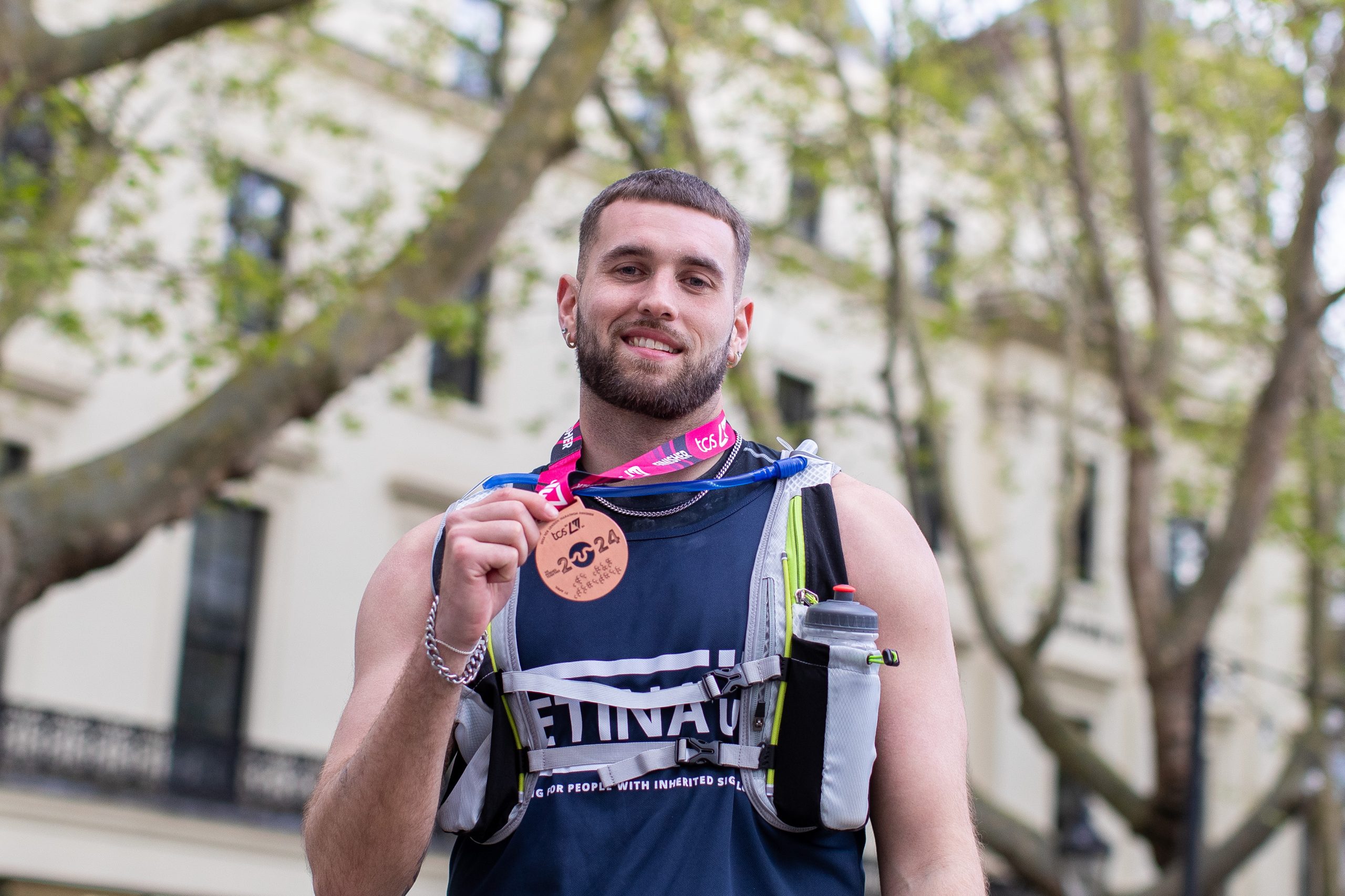 A male runner smiles as he holds his Marathon medal.