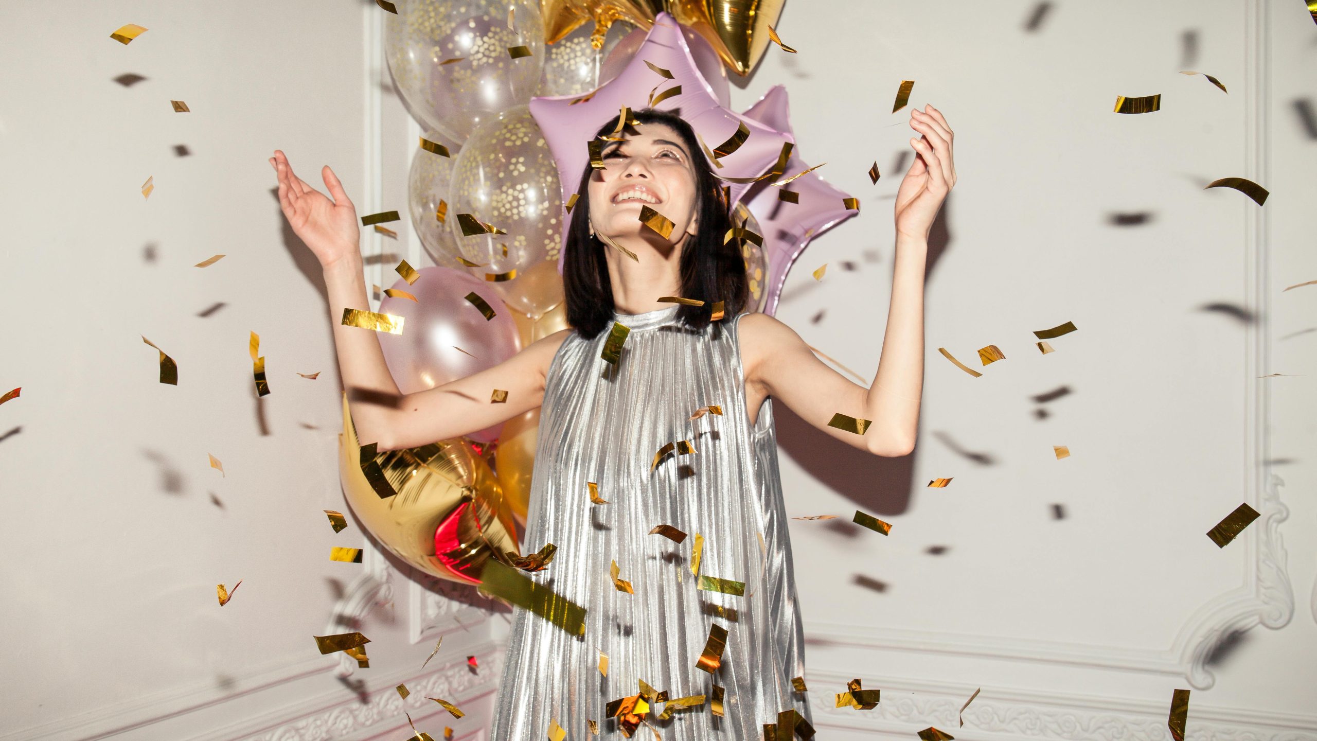 A young lady celebrates with confetti and balloons all around her.