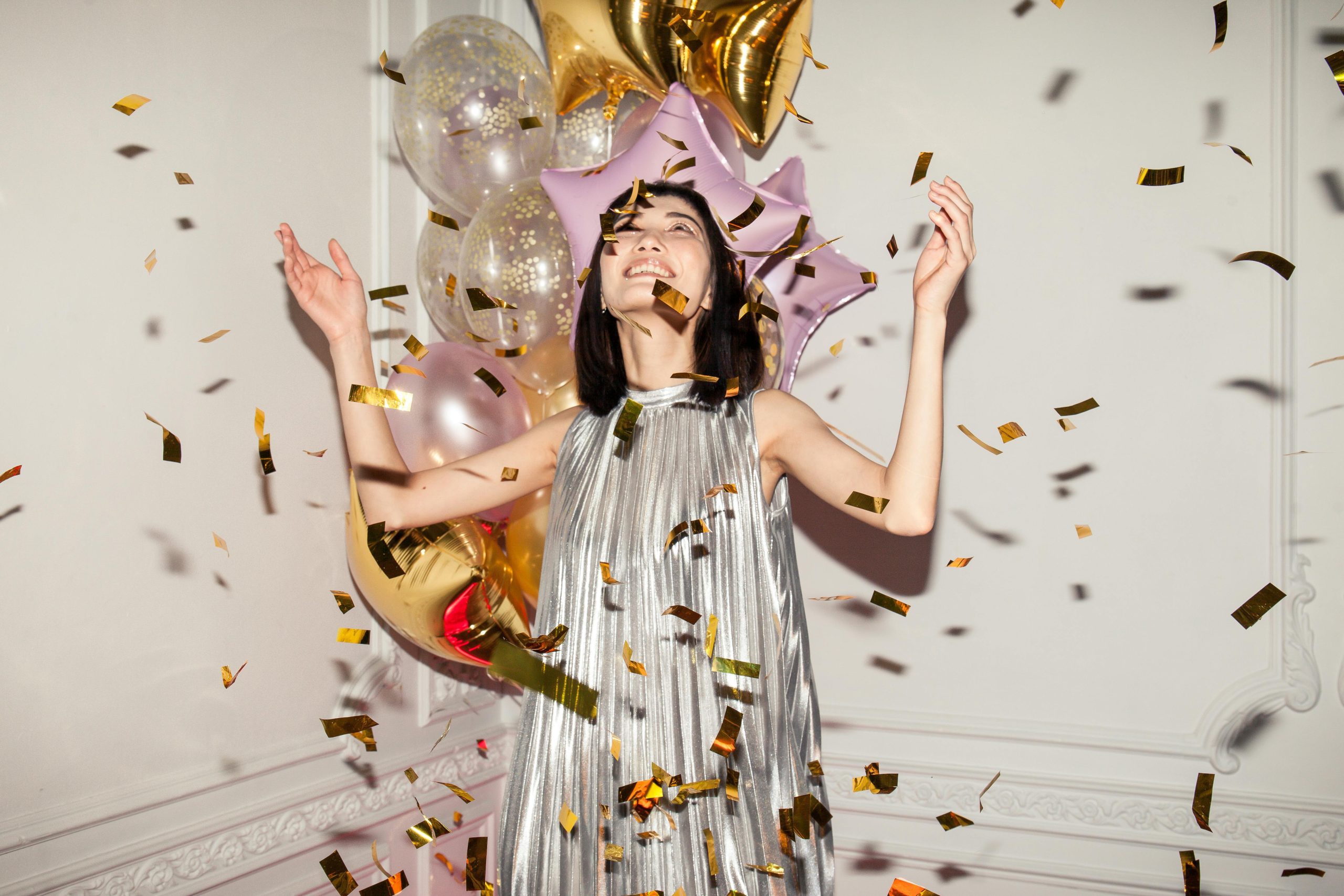 A young lady celebrates with confetti and balloons all around her.