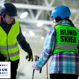 A ski instructor with student with high visibility jackets on with'Blind Skier' on the back