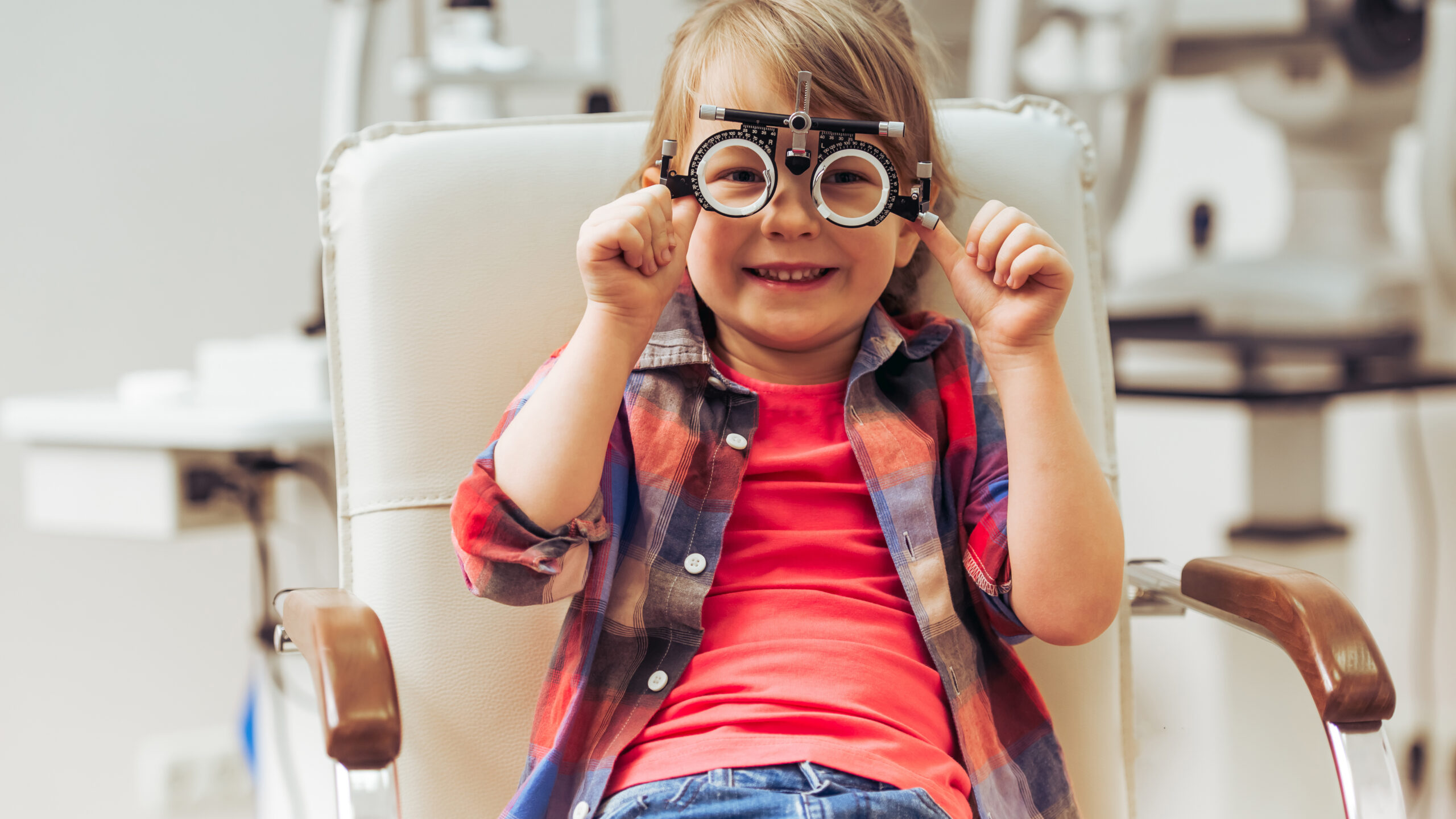 Little boy looking at camera and smiling while sitting on chair at the ophthalmologist