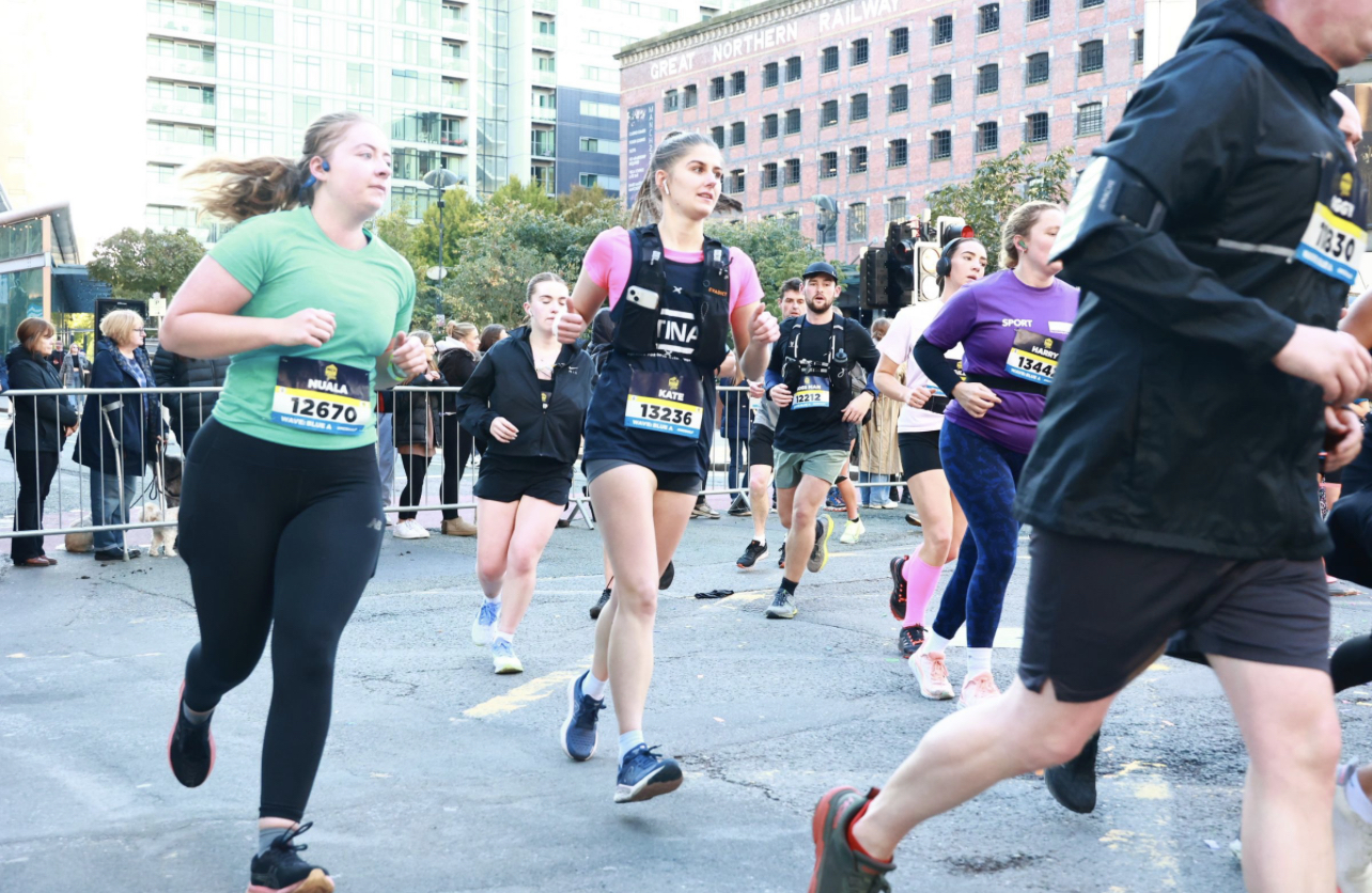 Several runners in a road race. Other runners and spectators line the street in the background.