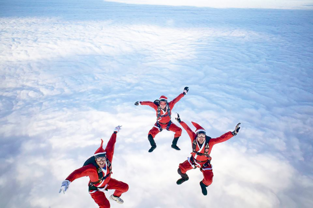 Three people skydiving dressed in red suits along with red hats