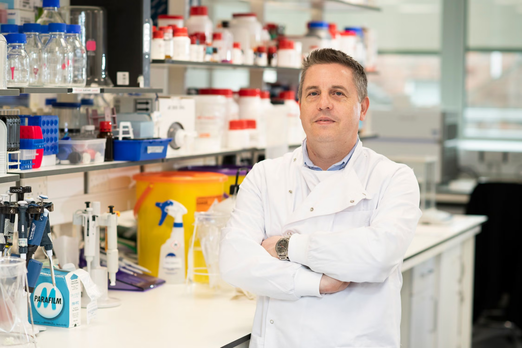 Professor Tim Curtis, lead researcher on the project, standing in a laboratory surrounded by scientific equipment and research materials.